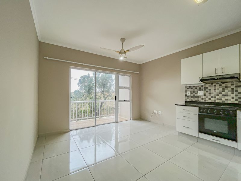An open-plan living and kitchen area featuring tiled floors, a ceiling fan, and direct access to a balcony through sliding glass doors.
