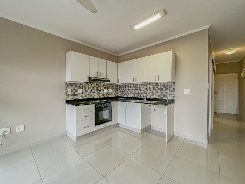 A clean, functional kitchen featuring white cabinetry, granite countertops, a mosaic tile backsplash, and built-in oven with extractor fan.