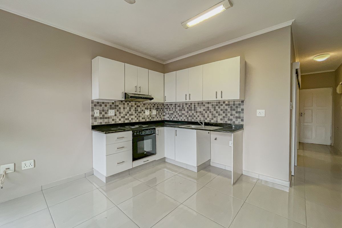 A clean, functional kitchen featuring white cabinetry, granite countertops, a mosaic tile backsplash, and built-in oven with extractor fan.