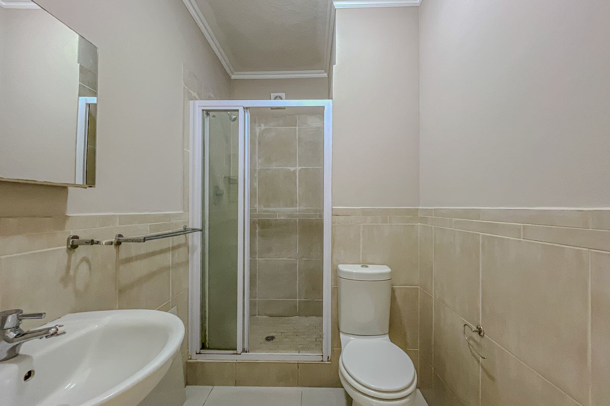 A functional bathroom featuring a shower enclosure, pedestal basin, and toilet with neutral wall and floor tiling.