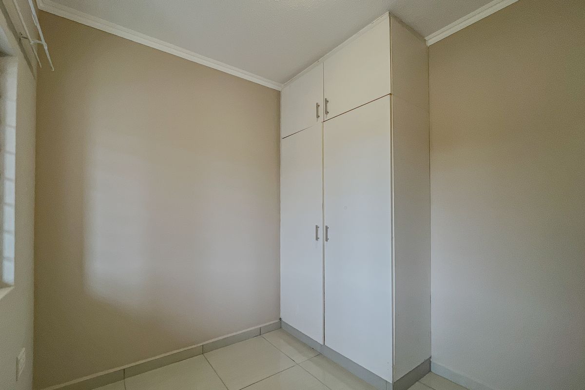 A clean, empty bedroom featuring neutral wall paint, tiled flooring, and a white built-in wardrobe with overhead storage.
