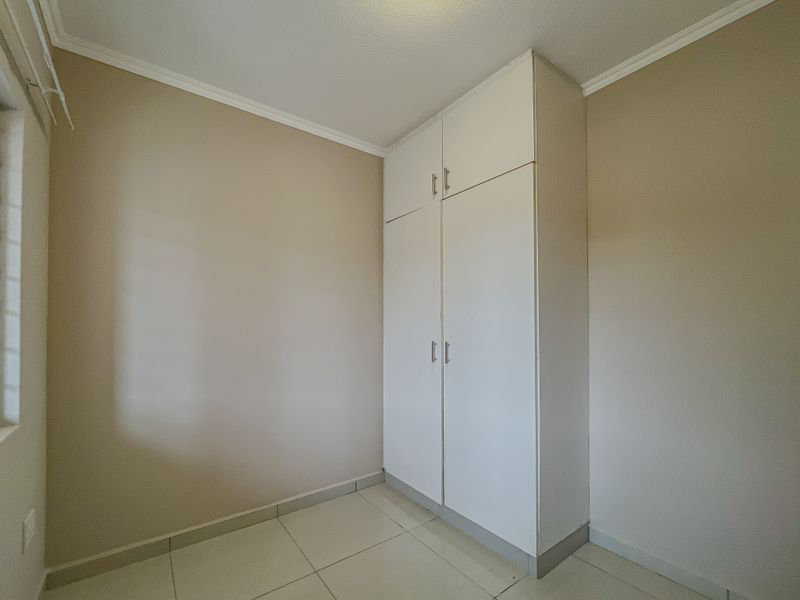 A clean, empty bedroom featuring neutral wall paint, tiled flooring, and a white built-in wardrobe with overhead storage.