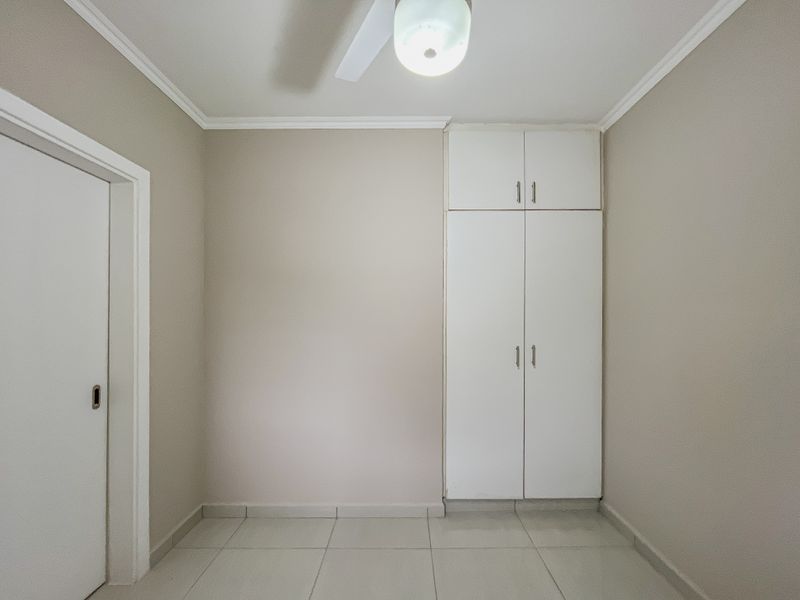 A clean, empty bedroom featuring neutral walls, tiled flooring, a ceiling fan, and built-in storage cupboards.