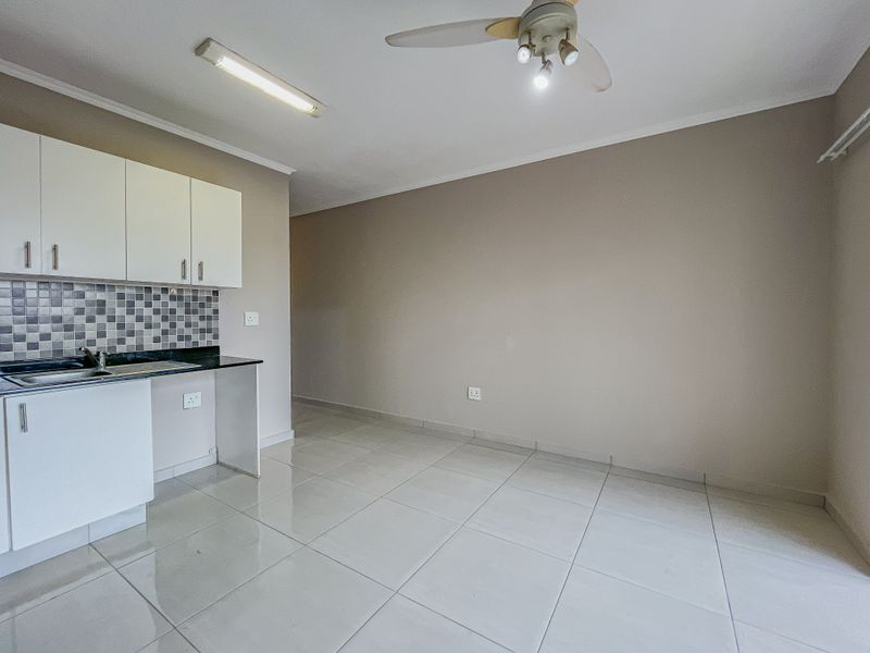 A compact, empty kitchen area featuring white cabinetry, a tiled splashback, and neutral floor tiles, ready for personalization.