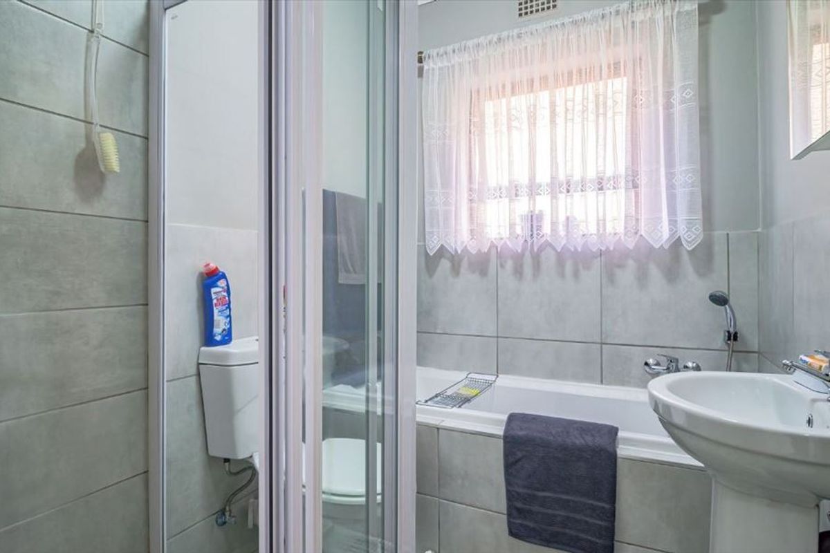 A functional bathroom featuring a shower enclosure, bathtub, pedestal basin, and toilet with neutral wall tiling.