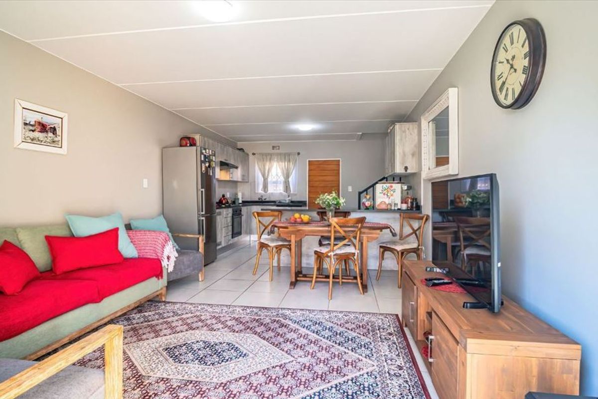 An open-plan living and dining area featuring tiled flooring and a functional kitchen space with built-in cabinetry and appliances.