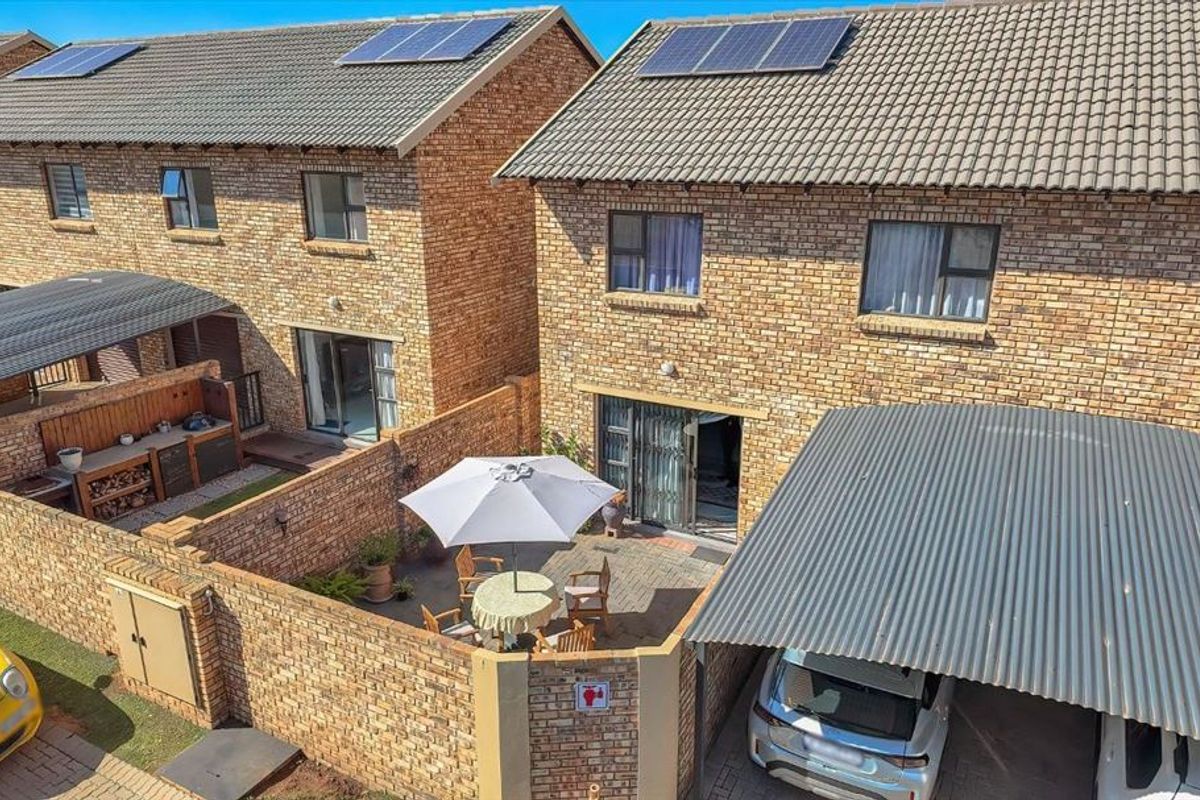 Aerial view of a townhouse rear exterior featuring a paved patio, private brick-walled courtyard, and a covered carport with solar panels on the roof.
