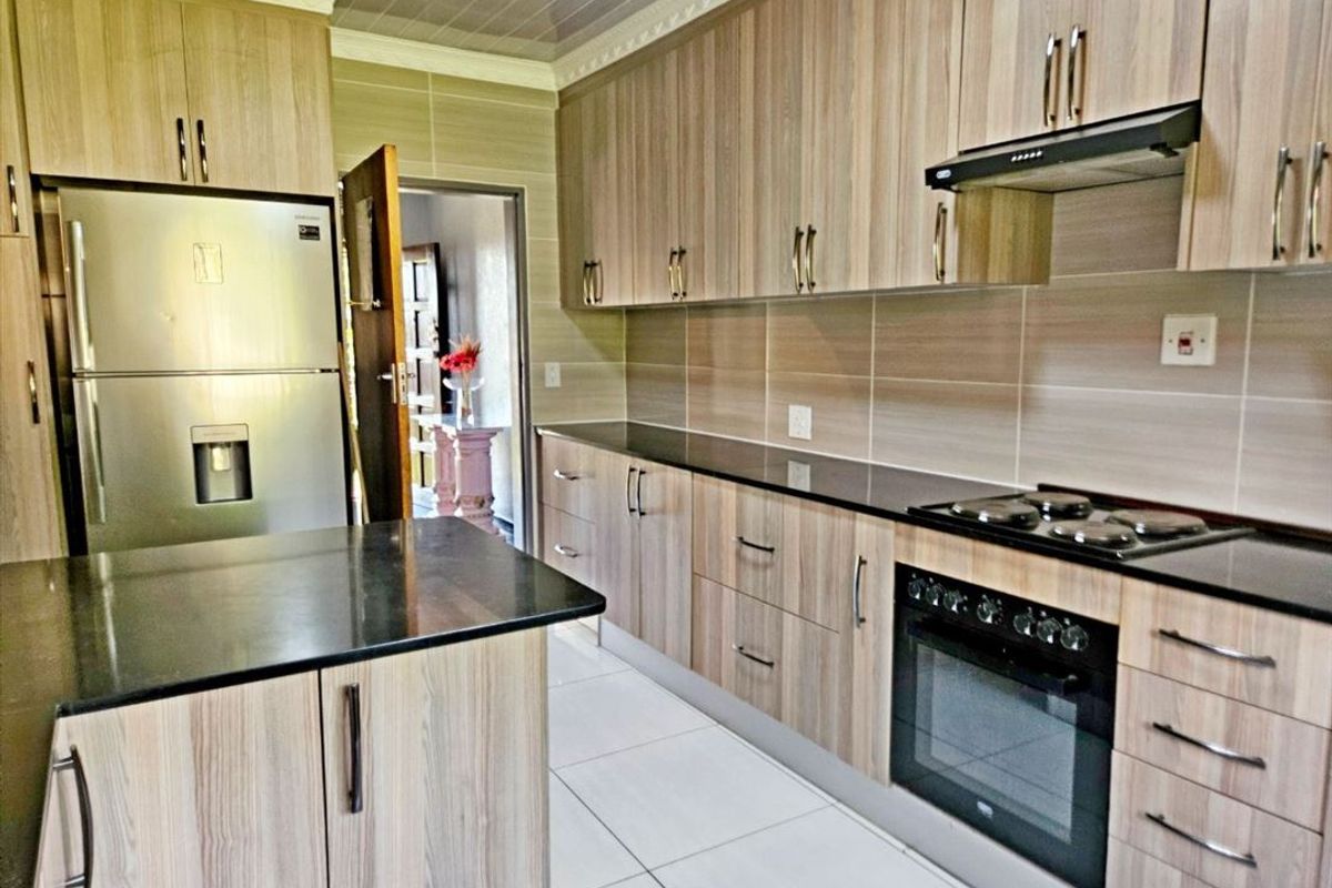 Modern kitchen featuring wood-grain cabinetry, black granite countertops, built-in oven, electric hob, extractor fan, and neutral tiled flooring.