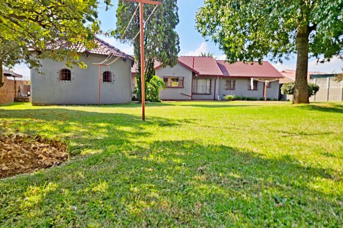 A spacious rear garden featuring a well-maintained lawn, mature trees, and a view of the rear building elevation with tiled roofing and security bars.
