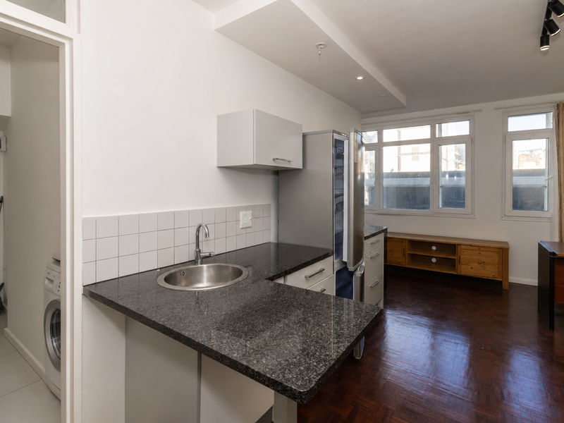 Open plan kitchen and living area featuring granite countertops, parquet flooring, and integrated cabinetry, with an adjacent laundry nook.