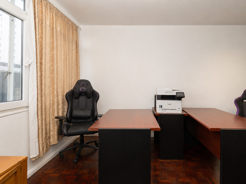 A functional home office space featuring classic parquet flooring and a large window providing natural light.