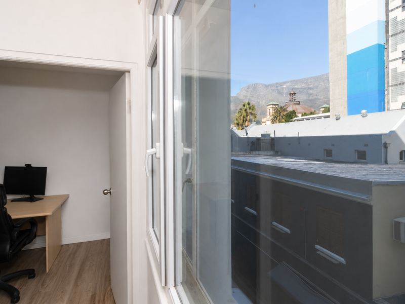A compact office space featuring laminate flooring and a window with an urban and mountain view.