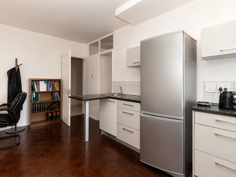 Open-plan kitchen area featuring white cabinetry, dark laminate countertops, tiled backsplash, and classic parquet flooring, seamlessly integrated with the living space.