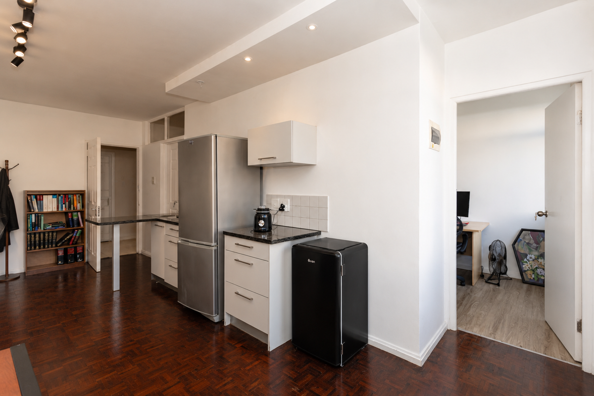 Compact kitchen area featuring parquet flooring, built-in cabinetry with stone countertops, tiled backsplash, and recessed ceiling lighting, adjacent to a separate room.