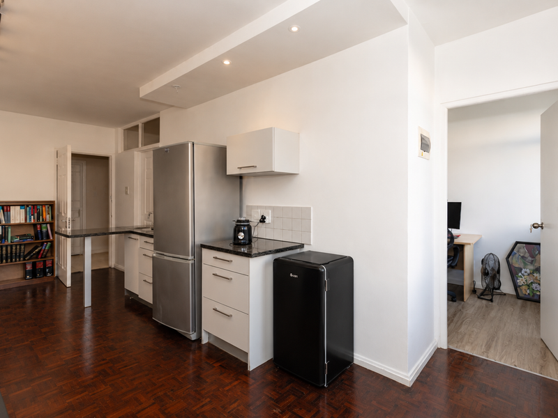 Compact kitchen area featuring parquet flooring, built-in cabinetry with stone countertops, tiled backsplash, and recessed ceiling lighting, adjacent to a separate room.