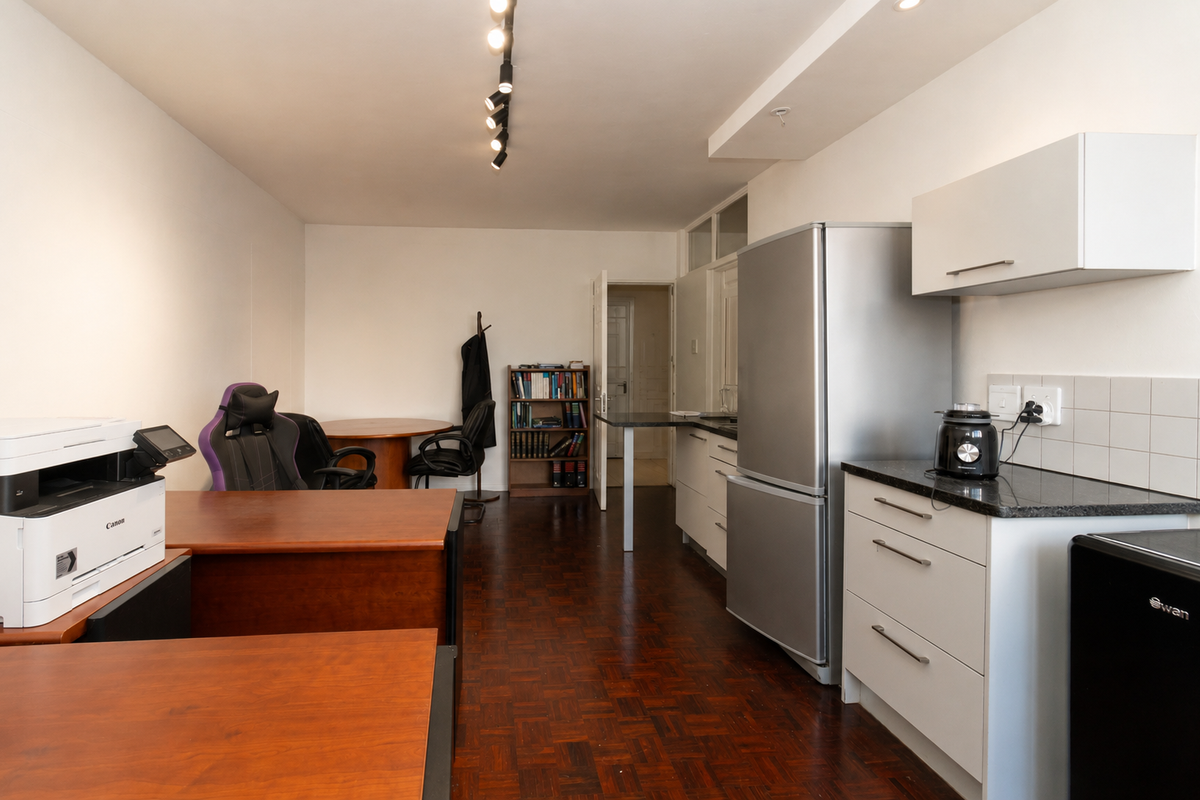 Open-plan living area featuring dark parquet flooring, track lighting, and a functional kitchen with white cabinetry and granite countertops.