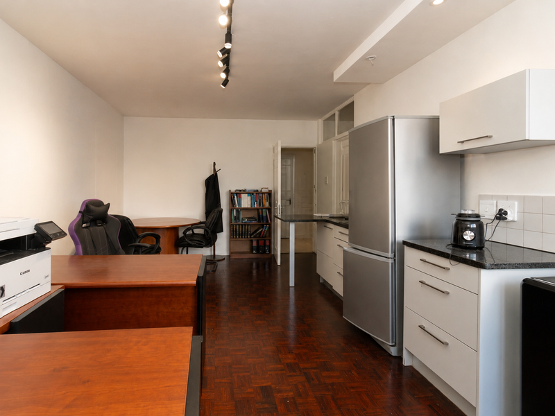 Open-plan living area featuring dark parquet flooring, track lighting, and a functional kitchen with white cabinetry and granite countertops.