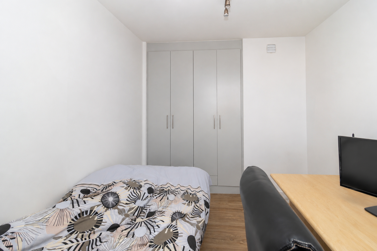A functional bedroom featuring light-toned laminate flooring and a neutral-colored built-in wardrobe providing ample storage space.