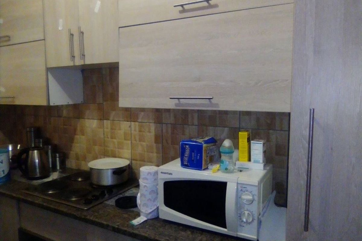 A functional kitchen area featuring light wood-finish cabinetry, a stone countertop, an electric hob, and a tiled backsplash.