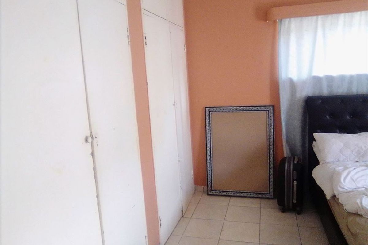 A bedroom featuring built-in cupboards and tiled flooring, currently showing signs of wear and requiring cosmetic updates.