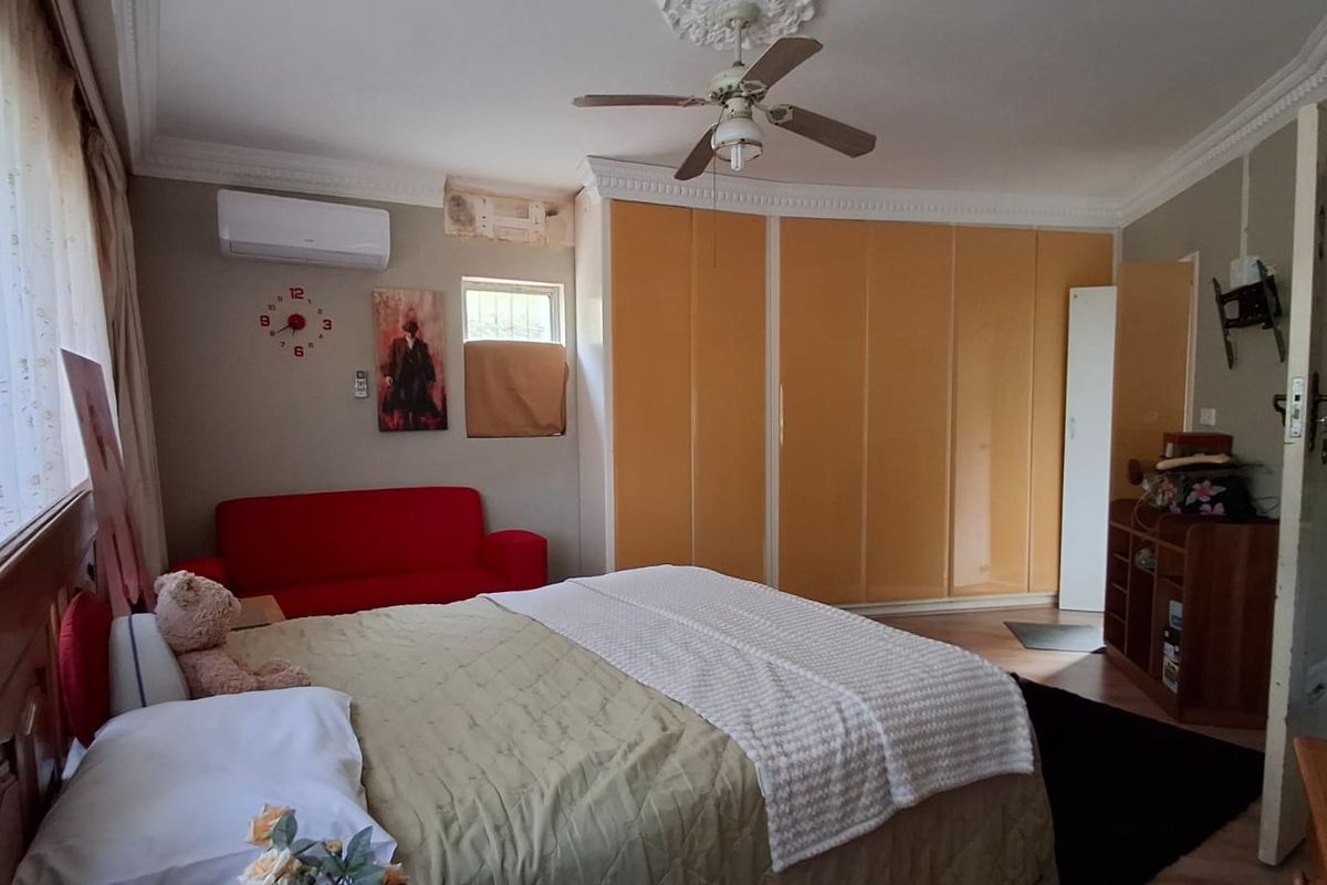 Spacious bedroom featuring built-in cupboards, a ceiling fan, and a wall-mounted air conditioning unit.