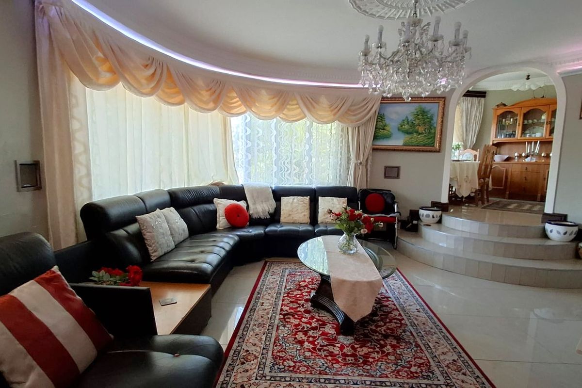 Spacious living room featuring a curved wall, recessed ceiling lighting, a crystal chandelier, and a raised platform area leading to the dining space.