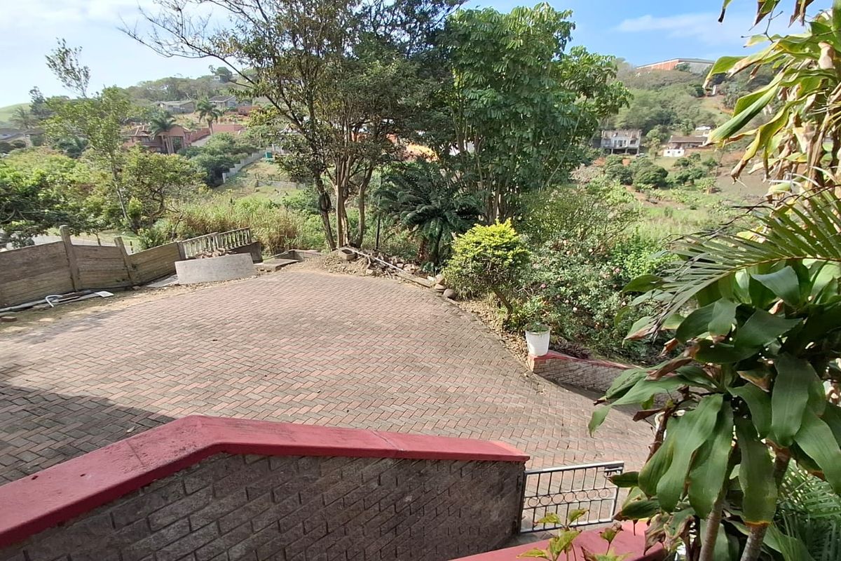 A paved rear driveway area featuring a retaining wall and views of the surrounding landscape and neighborhood.