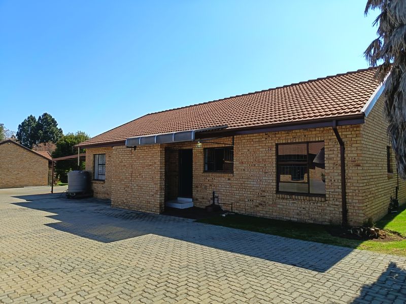 A well-maintained face brick townhouse exterior featuring a tiled roof, paved driveway, and aluminum window frames.