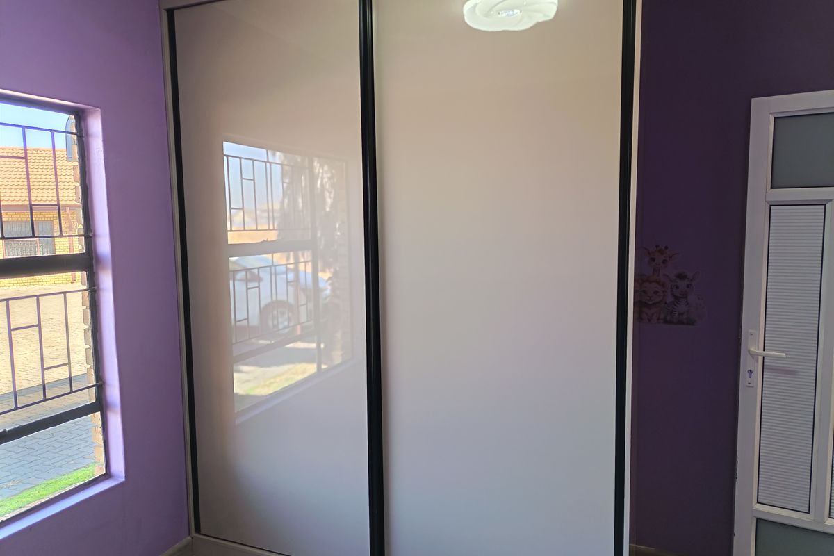 A bedroom featuring a modern built-in sliding door wardrobe, laminate flooring, and security bars on the window.