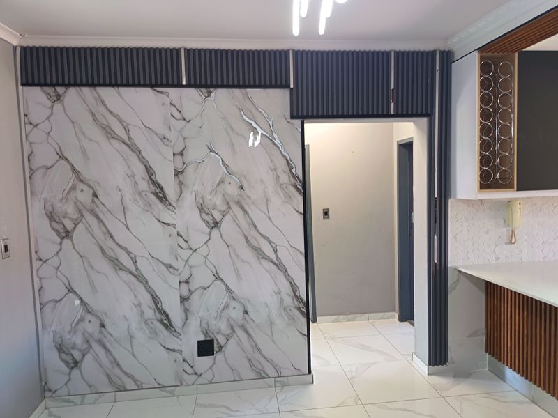 Modern kitchen area featuring marble-look wall paneling, slatted timber cabinetry, quartz countertops, and elegant hexagonal mosaic backsplash with high-quality porcelain floor tiles.