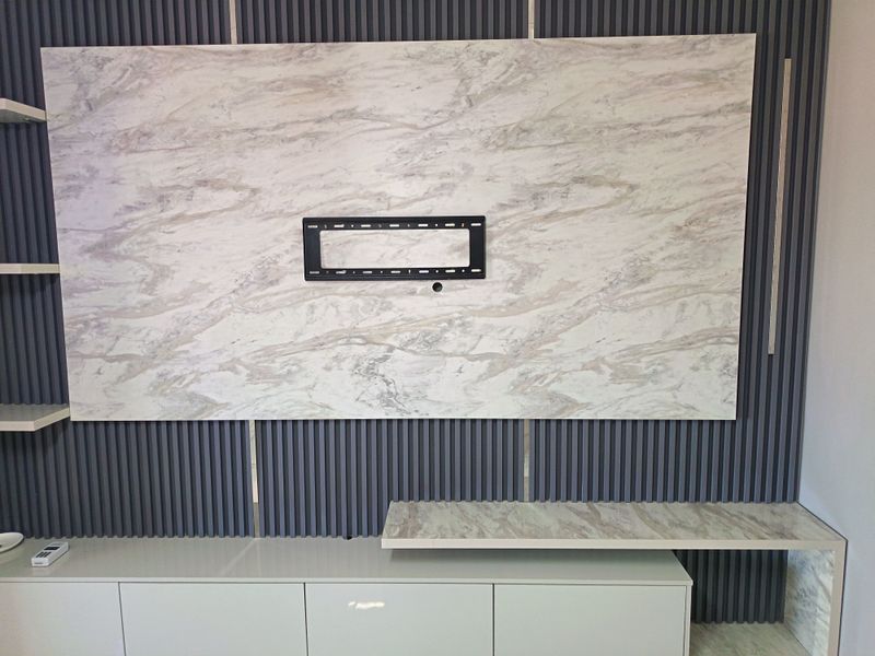 A modern living room feature wall with marble-effect paneling, integrated media console, slatted decorative wall accents, and built-in floating shelving.