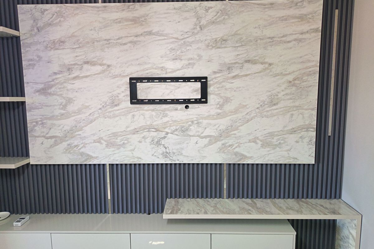 A modern living room feature wall with marble-effect paneling, integrated media console, slatted decorative wall accents, and built-in floating shelving.