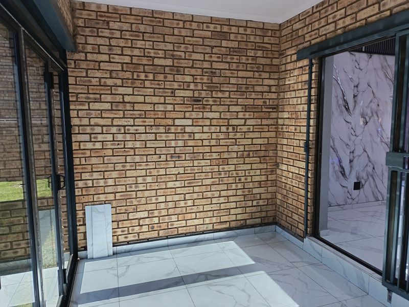 A bright, enclosed patio area featuring exposed brick walls, modern marble-look floor tiles, and large sliding glass doors providing access to the garden.
