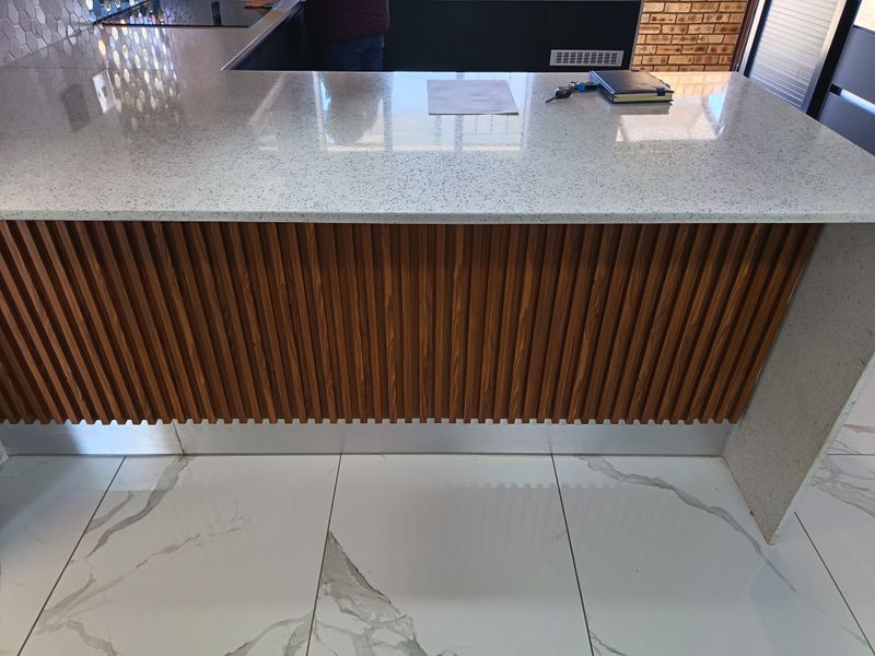 Modern kitchen island featuring a stone countertop, slatted wood detailing, and high-quality marble-look porcelain floor tiles.