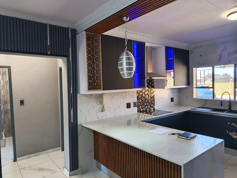 Modern kitchen featuring sleek dark cabinetry, quartz countertops, a stylish hexagonal mosaic backsplash, and decorative slatted wood detailing with integrated lighting.