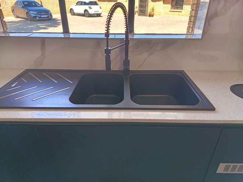 A modern kitchen area featuring a double bowl sink with a black gooseneck mixer tap, set into a quartz countertop with marble-look splashback tiles.