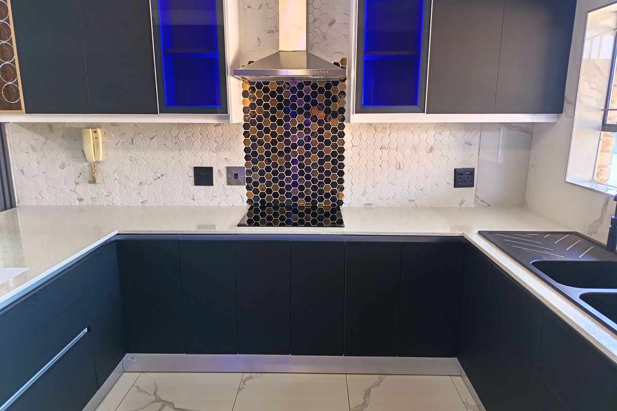 Modern kitchen featuring dark cabinetry, quartz countertops, a striking hexagonal mosaic backsplash, integrated hob, and high-quality marble-look floor tiles.