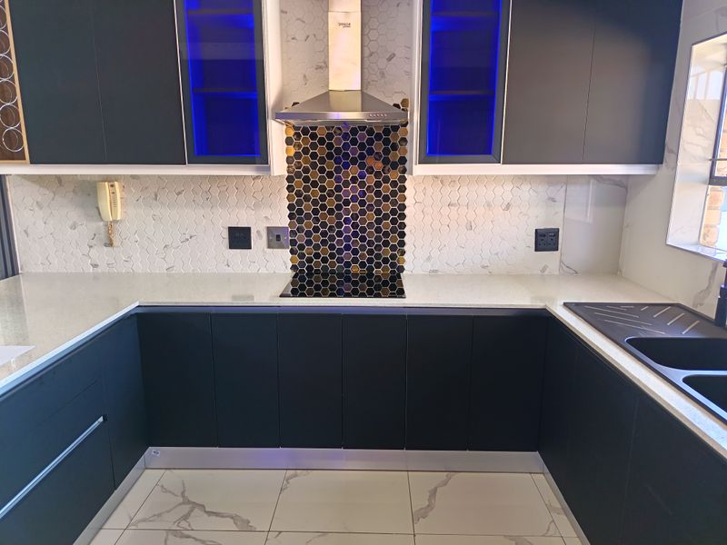 Modern kitchen featuring dark cabinetry, quartz countertops, a striking hexagonal mosaic backsplash, integrated hob, and high-quality marble-look floor tiles.