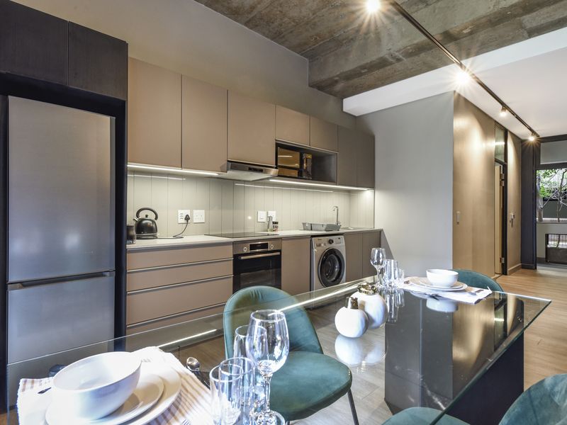 Modern open-plan kitchen featuring sleek cabinetry, integrated appliances, and an exposed concrete ceiling, seamlessly flowing into the dining area.
