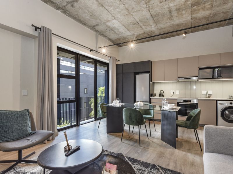 Modern open-plan living area featuring an exposed concrete ceiling, sleek cabinetry, integrated kitchen appliances, and large sliding doors leading to a balcony.