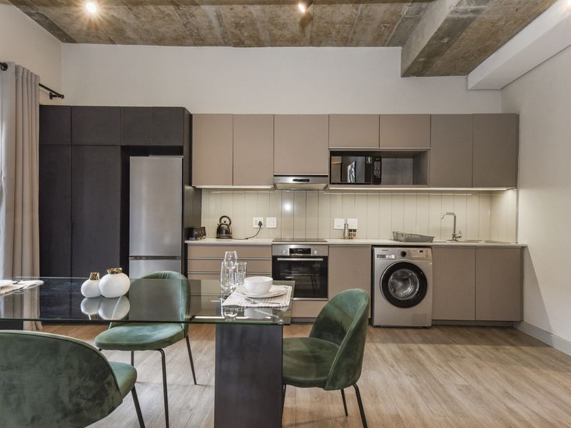 Modern open-plan kitchen featuring sleek cabinetry, integrated appliances, and an exposed concrete ceiling, seamlessly flowing into the dining area.