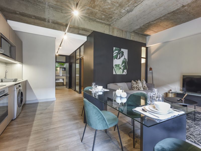 Modern open-plan apartment featuring an industrial-style exposed concrete ceiling, sleek kitchen cabinetry, and integrated appliances, flowing into a contemporary dining and living area.