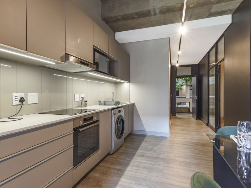 Modern kitchen featuring sleek cabinetry, stone countertops, integrated appliances, and an exposed concrete ceiling, seamlessly flowing into the adjacent living area.