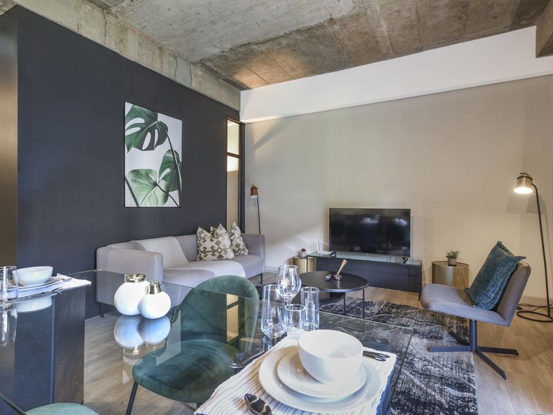 Modern open-plan living and dining area featuring an industrial-style exposed concrete ceiling, laminate flooring, and a striking dark accent wall.