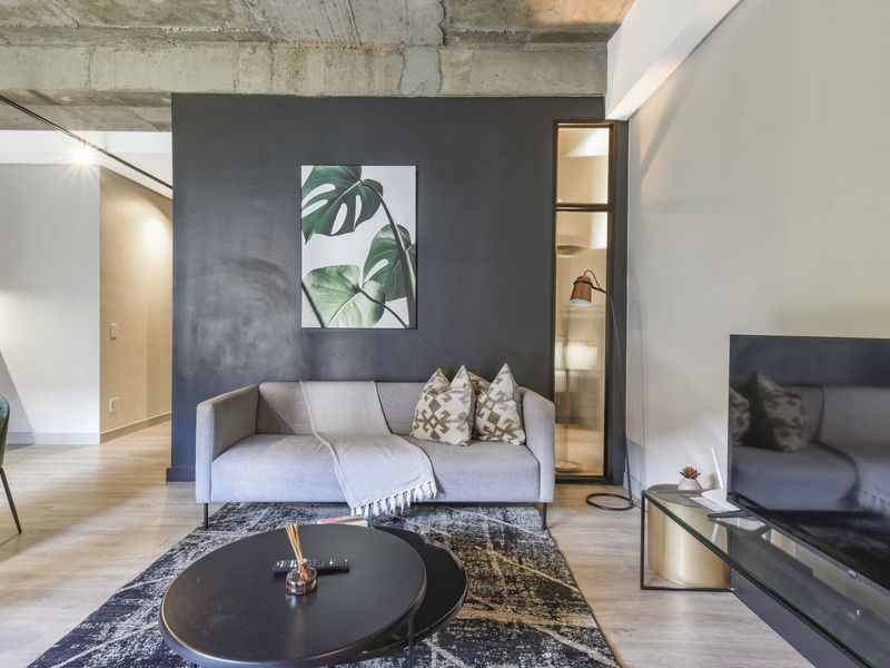 Modern living room featuring an exposed concrete ceiling, sleek dark accent wall, and a stylish fluted glass partition.