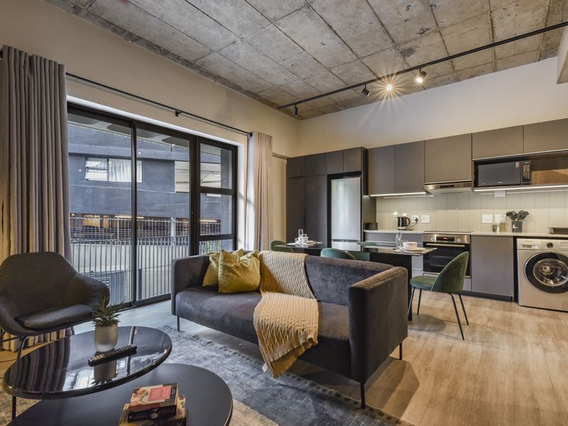 Modern open-plan apartment featuring an exposed concrete ceiling, sleek kitchen cabinetry with integrated appliances, and large sliding doors leading to a balcony.