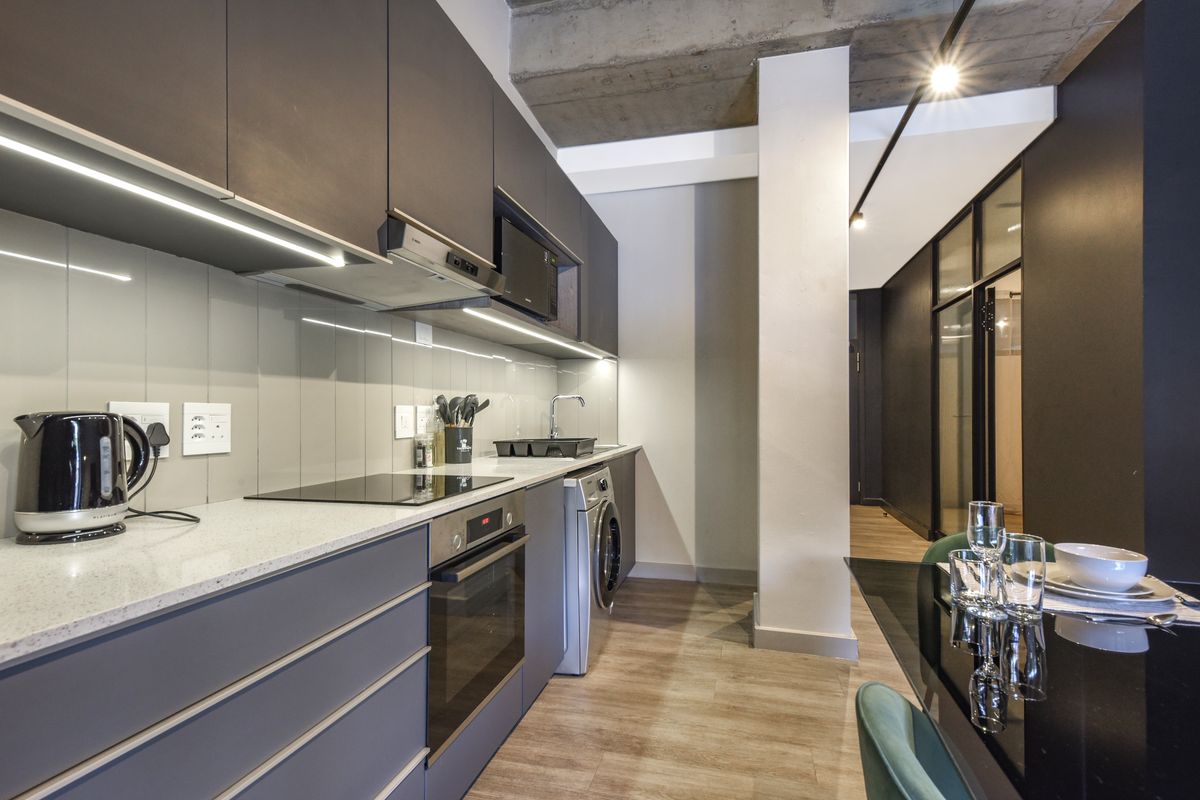 Modern kitchen featuring sleek dark cabinetry, stone countertops, integrated appliances, and an industrial-style exposed concrete ceiling, seamlessly flowing into the dining area.