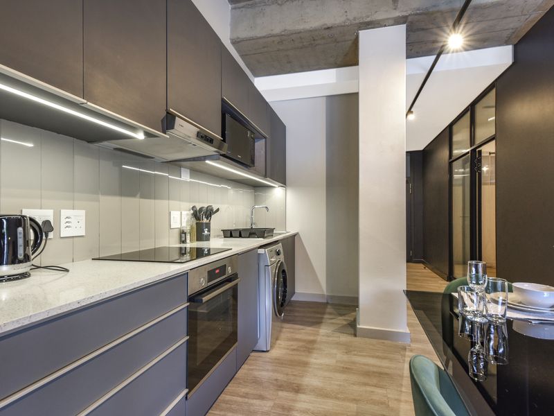 Modern kitchen featuring sleek dark cabinetry, stone countertops, integrated appliances, and an industrial-style exposed concrete ceiling, seamlessly flowing into the dining area.