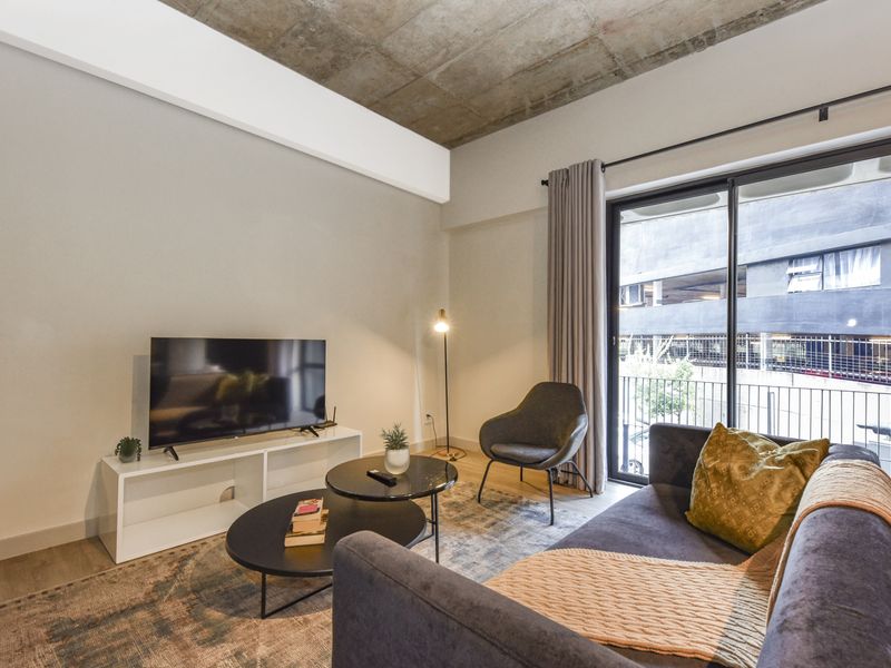 Modern living room featuring an exposed concrete ceiling, neutral walls, and a large sliding glass door providing access to a private balcony.