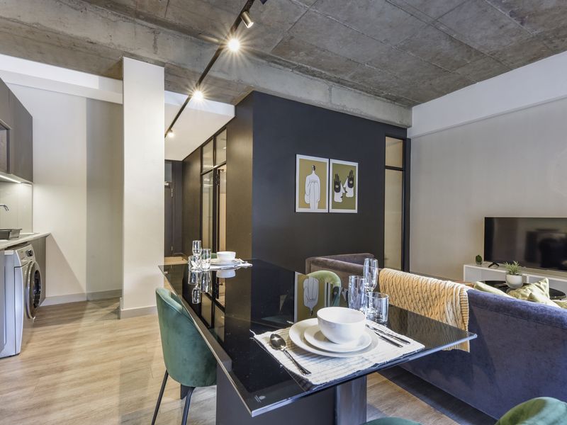 Modern open-plan living area featuring an exposed concrete ceiling, sleek kitchen cabinetry with integrated appliances, and contemporary track lighting.